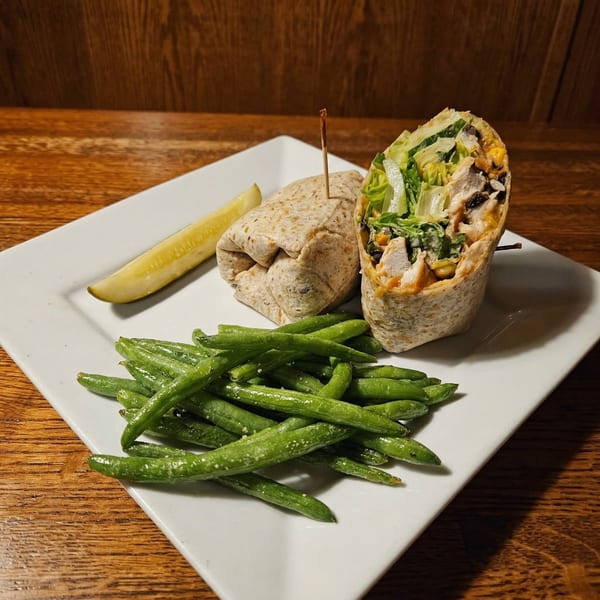 Chicken wrap with lettuce, corn, and black beans, served with green beans and a pickle spear.